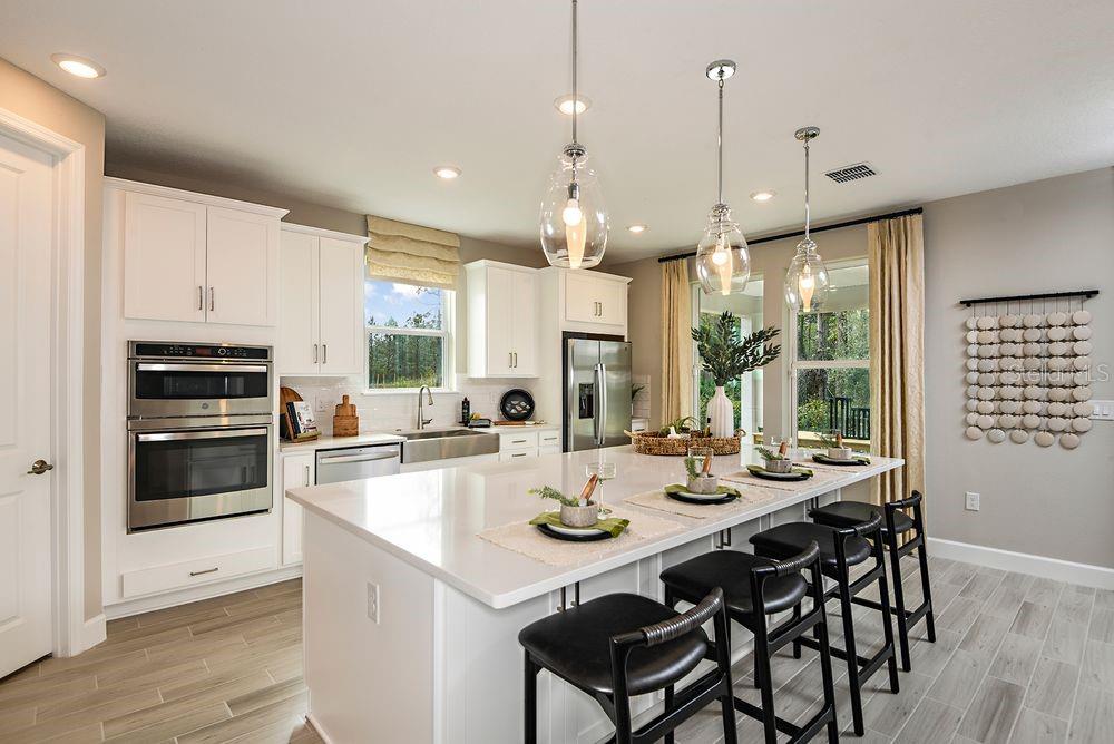 A modern kitchen features white cabinetry, a large quartz island, and three glass pendant lights — 5 ARMENIA COURT, PALM COAST, FL