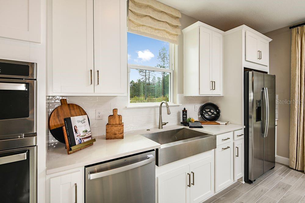 A kitchen features white cabinets, stainless steel appliances, a farmhouse sink, and a window view — 5 ARMENIA COURT, PALM COAST, FL