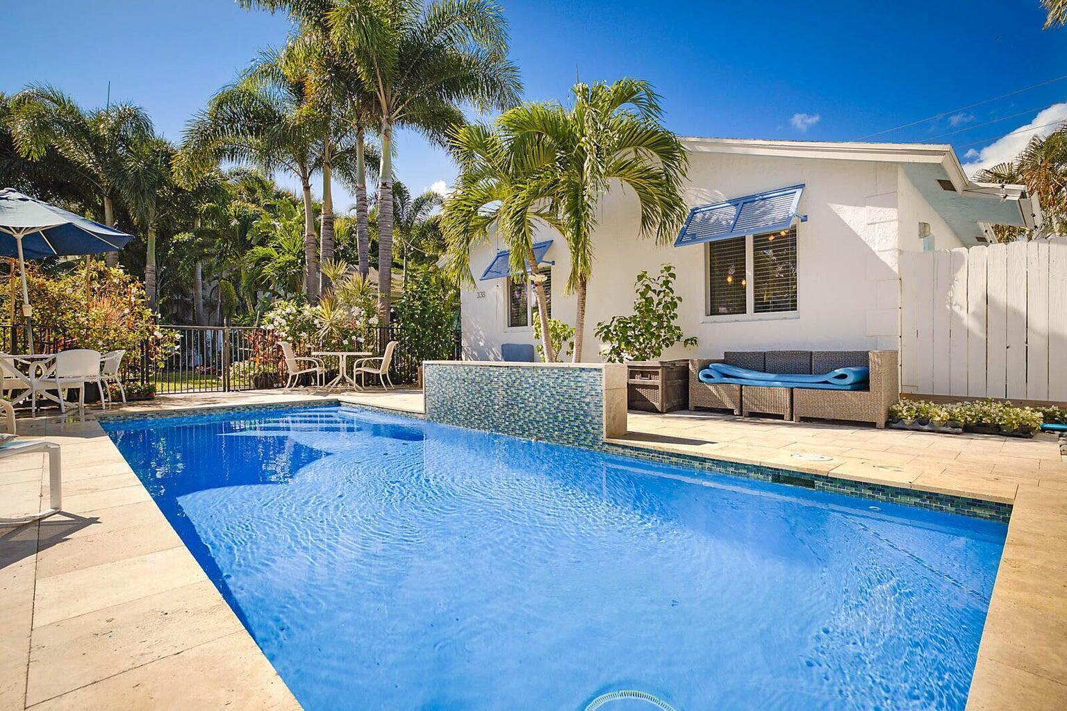 A swimming pool with a tiled water feature sits beside a white house with palm trees — 334 NE 7th Avenue, Delray Beach FL 33483, DELRAY BEACH, FL