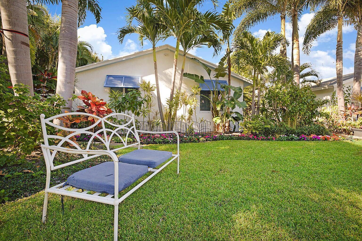 A white metal bench sits on a green lawn in front of a tropical house — 334 NE 7th Avenue, Delray Beach FL 33483, DELRAY BEACH, FL