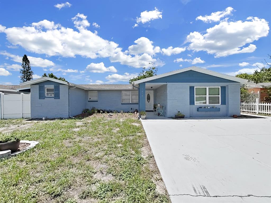 A single-story blue brick house features a concrete driveway and a white front door — 3424 TRUMAN DRIVE, HOLIDAY, FL