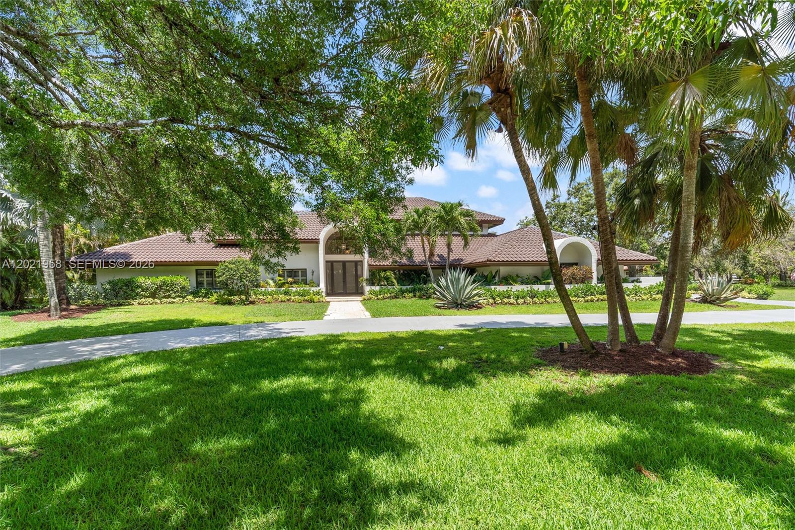 A large single-story house with a tiled roof and arched entryway sits behind a lawn — 7011 Hialeah Ln, Parkland FL 33067, PARKLAND, FL