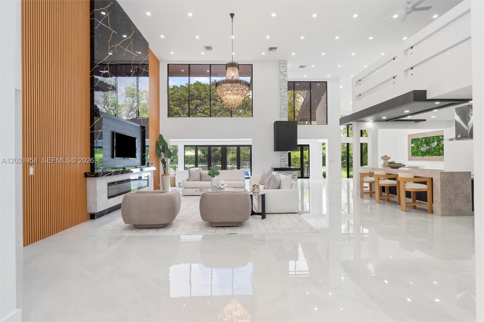 A spacious, modern living room features high ceilings, a marble fireplace, and a large chandelier — 7011 Hialeah Ln, Parkland FL 33067, PARKLAND, FL