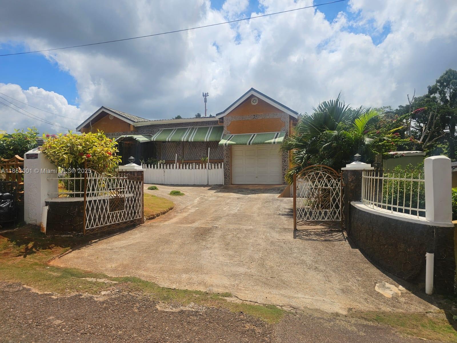 A single-story house with a concrete driveway, white metal gates, and green striped awnings — 00 Mandeville, Manchester Hills Jamaica, FL, FL