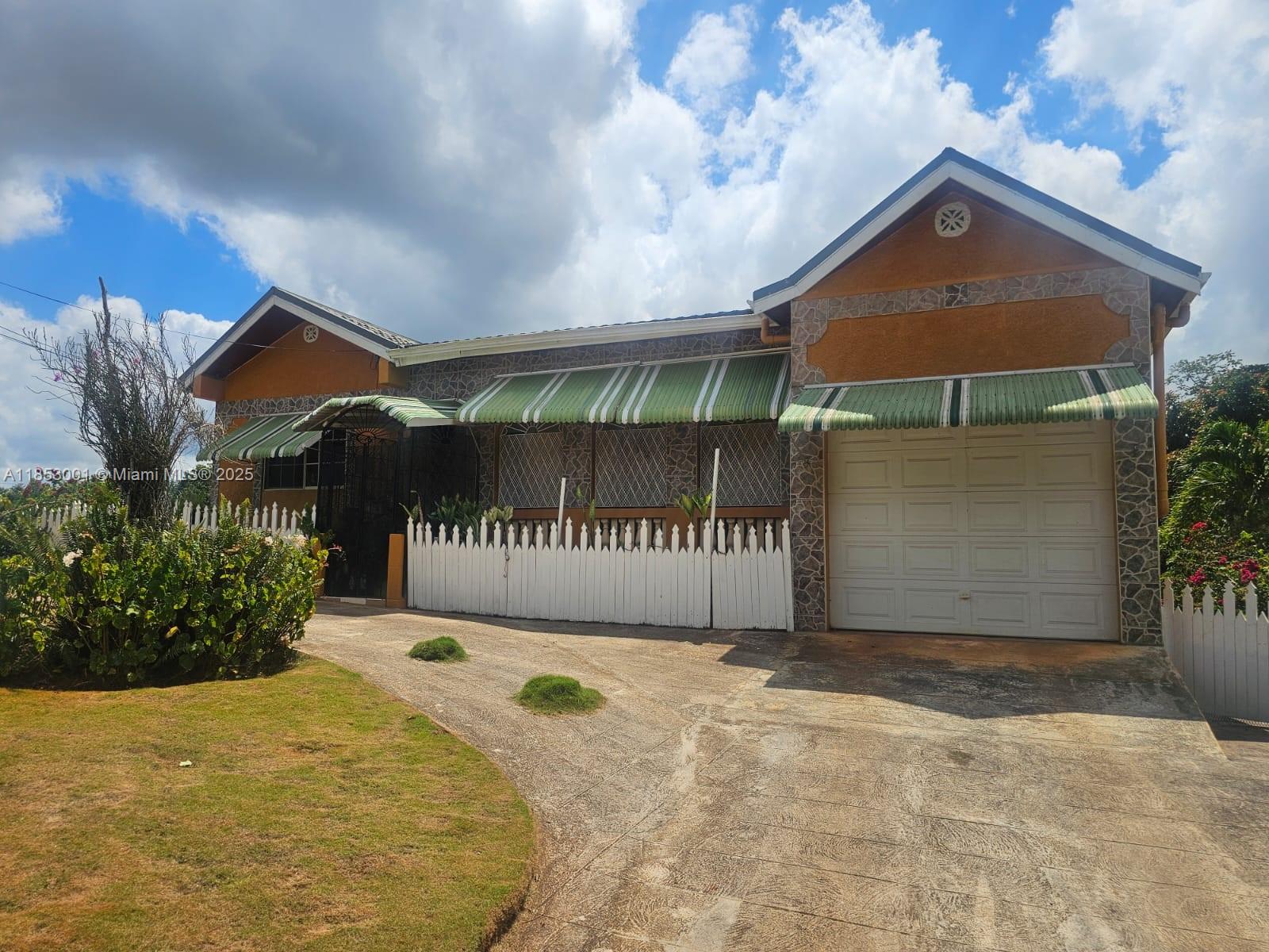 A single-story house with a white picket fence, green striped awnings, and a concrete driveway — 00 Mandeville, Manchester Hills Jamaica, FL, FL