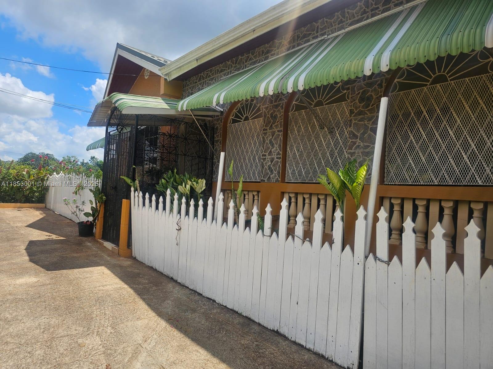 A white picket fence runs along the side of a house with stone-patterned exterior walls — 00 Mandeville, Manchester Hills Jamaica, FL, FL