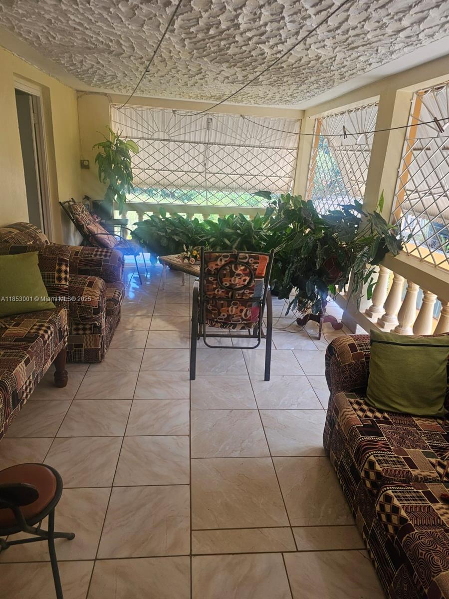 A covered patio features tiled floors, patterned furniture, and a textured ceiling — 00 Mandeville, Manchester Hills Jamaica, FL, FL
