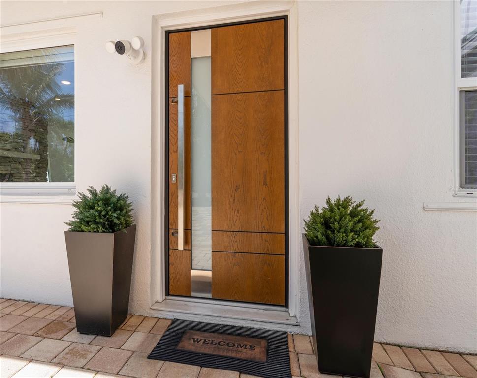 A modern wood-paneled front door with a vertical glass insert sits between two tall planters — 1854 VENETIAN POINT DRIVE, CLEARWATER, FL