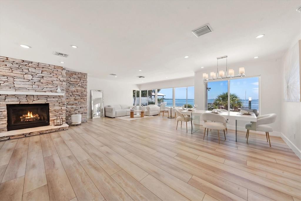 A bright living and dining area features a stone fireplace, light wood floors, and water views — 1854 VENETIAN POINT DRIVE, CLEARWATER, FL