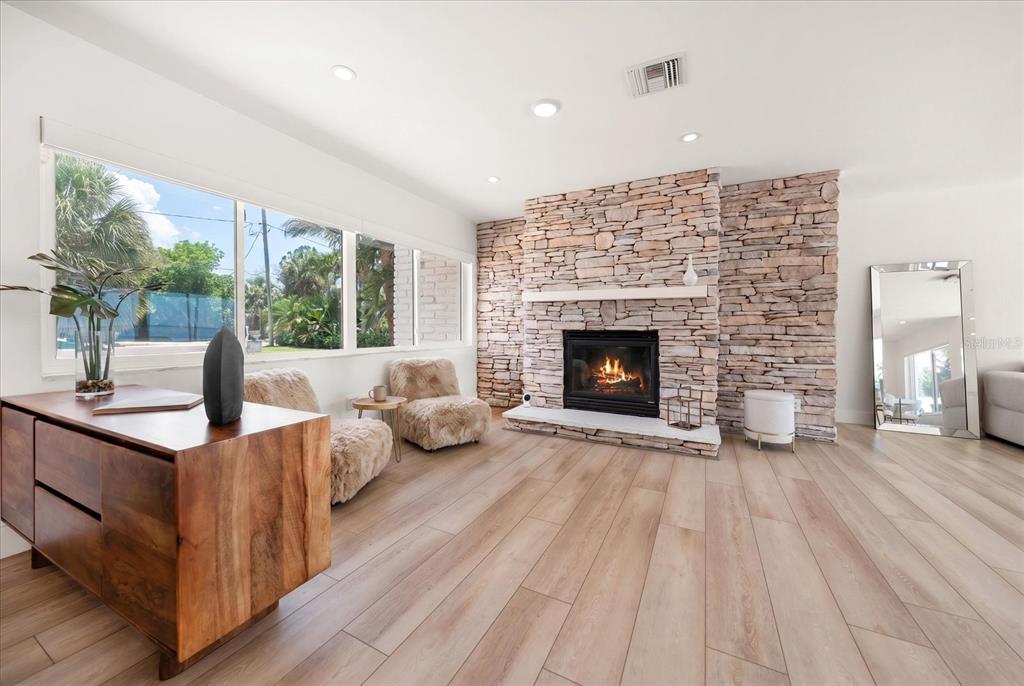 A living room features a stone fireplace, light wood flooring, and large windows with outdoor views — 1854 VENETIAN POINT DRIVE, CLEARWATER, FL