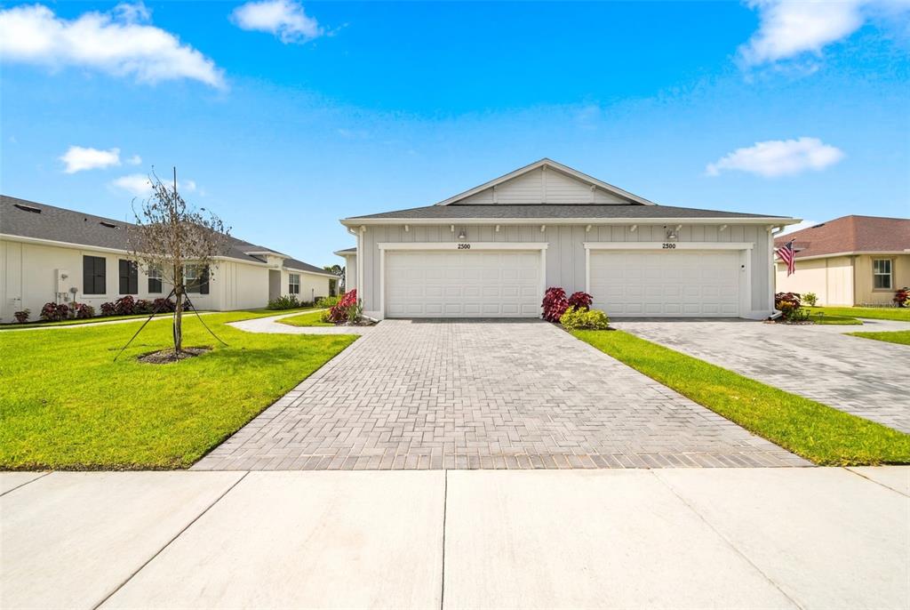 A light-colored duplex features two garage doors, a paver driveway, and a grassy lawn — 2286 CERULEAN DRIVE NW, PALM BAY, FL
