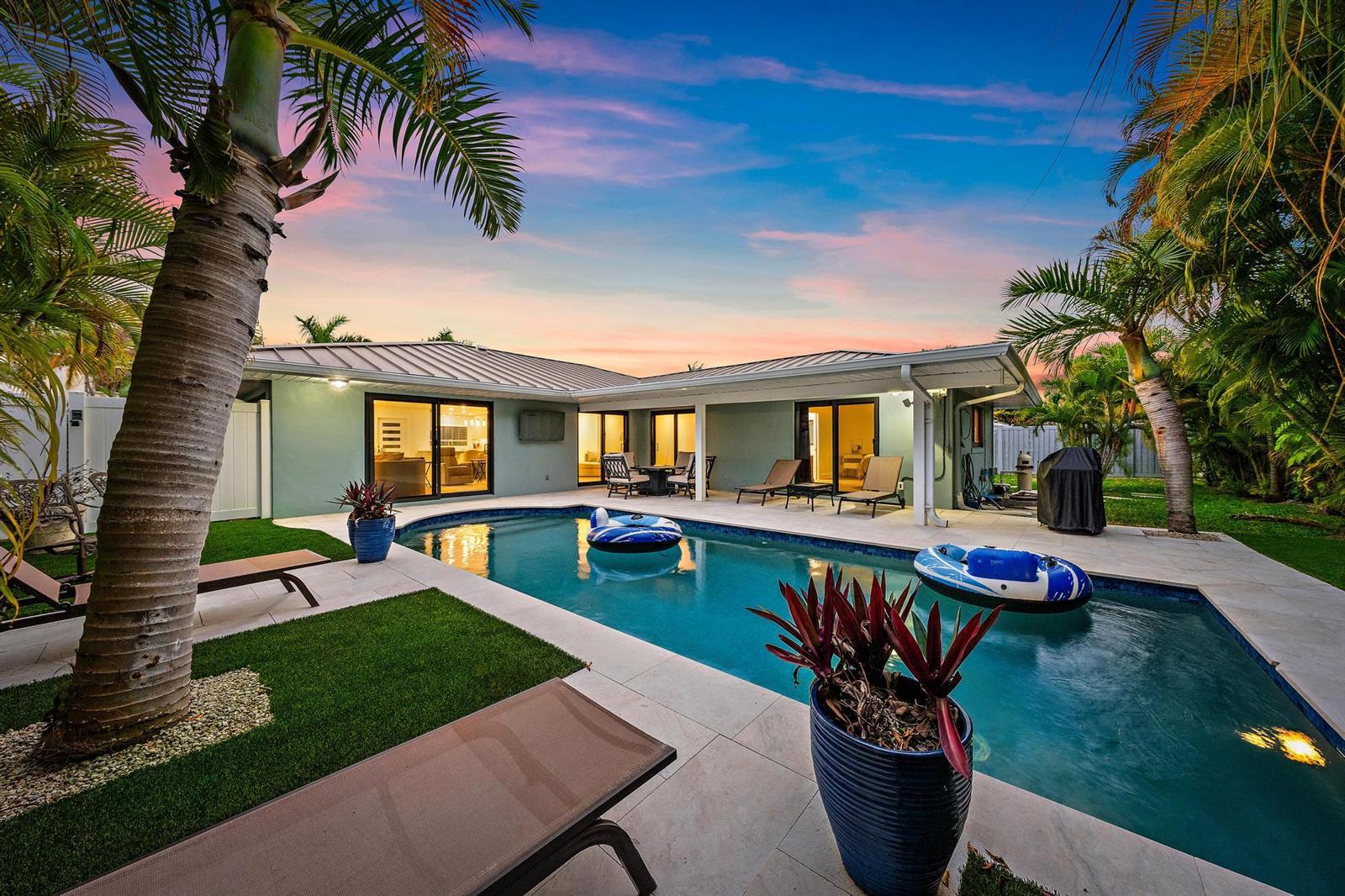 A backyard features a swimming pool, lounge chairs, palm trees, and a single-story house exterior — 1120 Singer Drive, Riviera Beach FL 33404, RIVIERA BEACH, FL