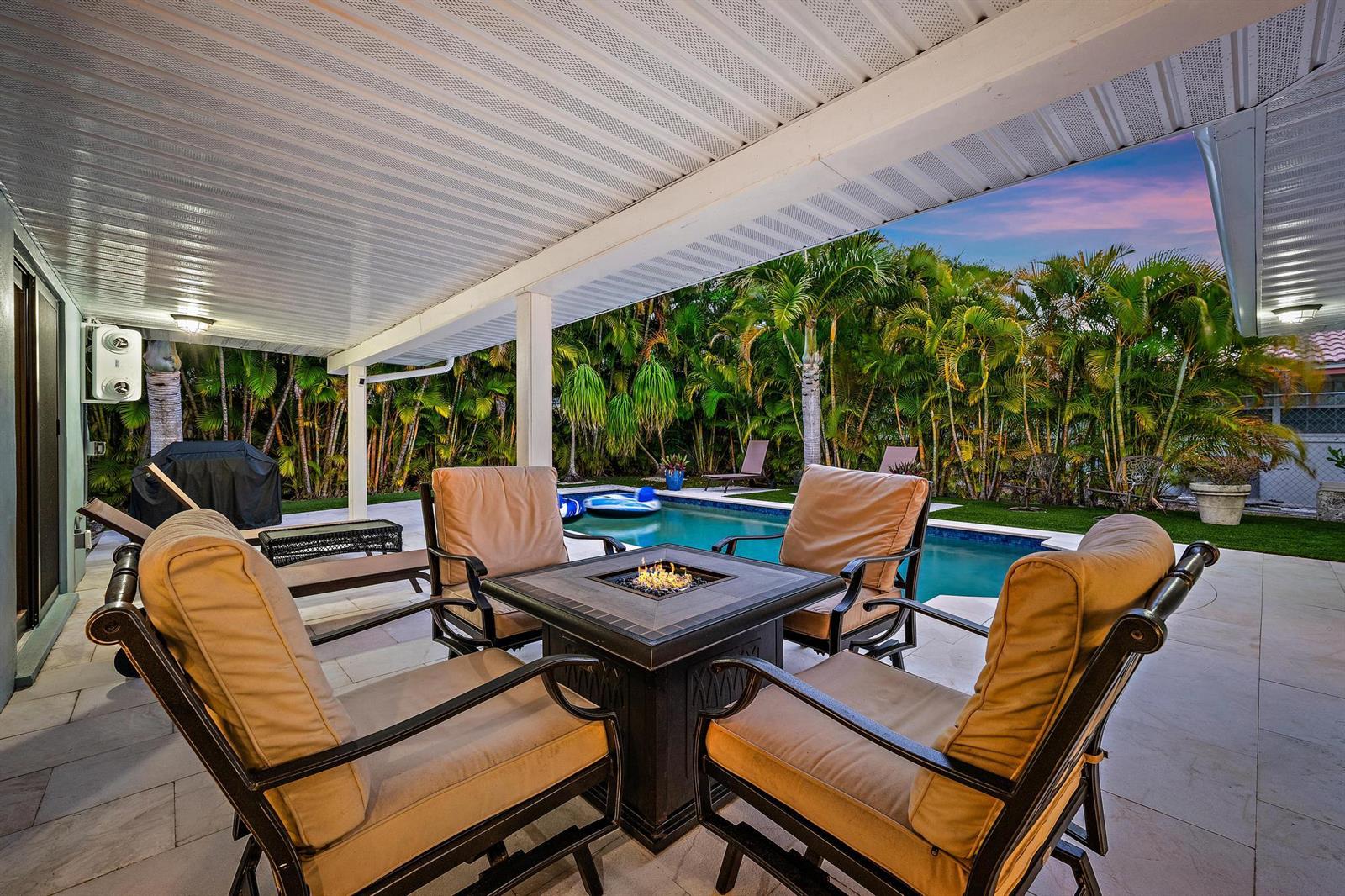 A covered patio features a fire pit, four chairs, and a view of a swimming pool — 1120 Singer Drive, Riviera Beach FL 33404, RIVIERA BEACH, FL