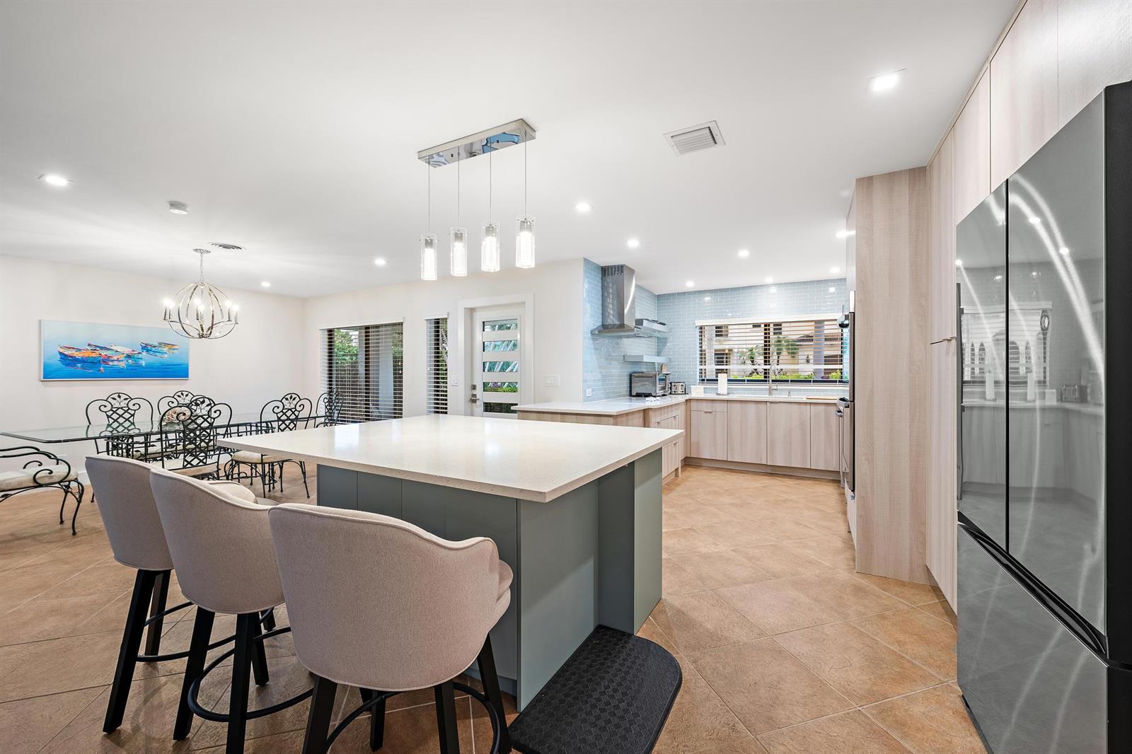 A kitchen and dining area features a central island, light wood cabinets, and tile flooring — 1120 Singer Drive, Riviera Beach FL 33404, RIVIERA BEACH, FL