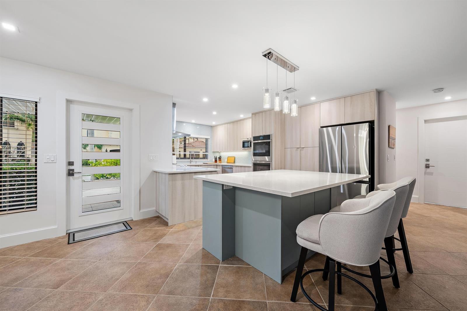 A modern kitchen features a blue island, light wood cabinetry, and stainless steel appliances — 1120 Singer Drive, Riviera Beach FL 33404, RIVIERA BEACH, FL