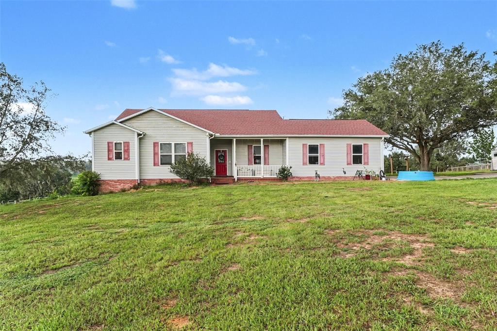 A single-story house with light siding, a red roof, and a red front door — 36304 TOMKOW LANE, DADE CITY, FL