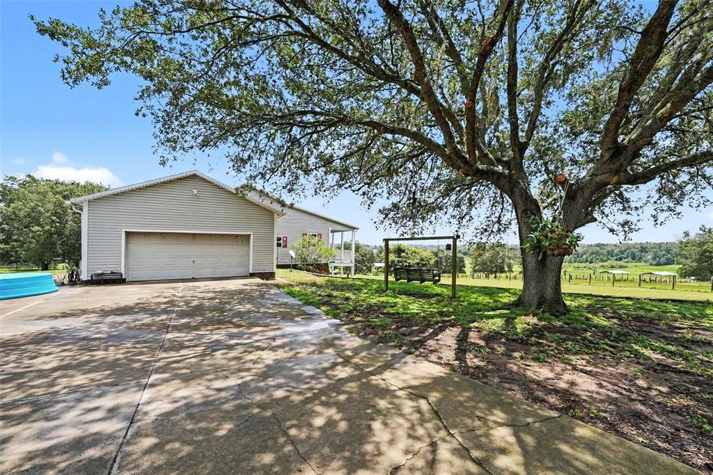 A concrete driveway leads to a garage beside a large tree with a porch swing — 36304 TOMKOW LANE, DADE CITY, FL