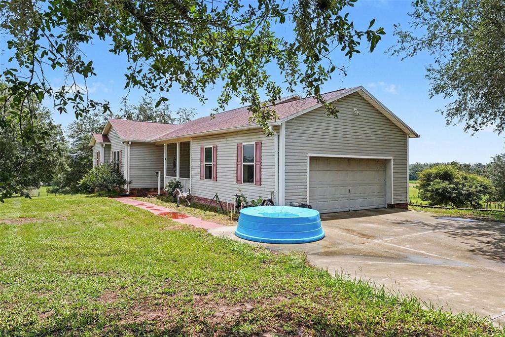 A single-story house with light gray siding, a two-car garage, and a blue plastic pool — 36304 TOMKOW LANE, DADE CITY, FL