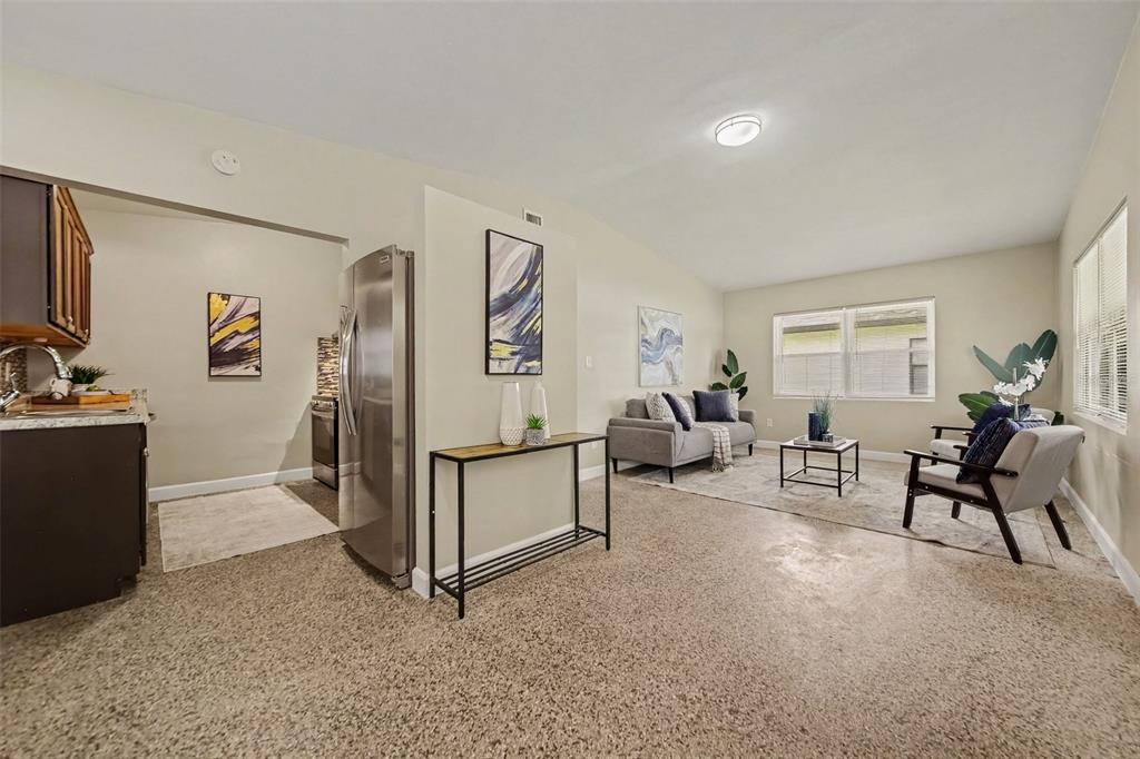 A living room with beige walls and speckled flooring connects to a kitchen area — 4965 ORANGE AVENUE, WINTER PARK, FL