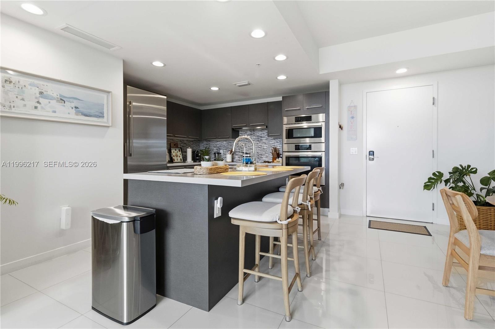 A modern kitchen features dark cabinetry, stainless steel appliances, a central island, and white flooring — 7875 NW 107th Ave # 310, Doral FL 33178, DORAL, FL