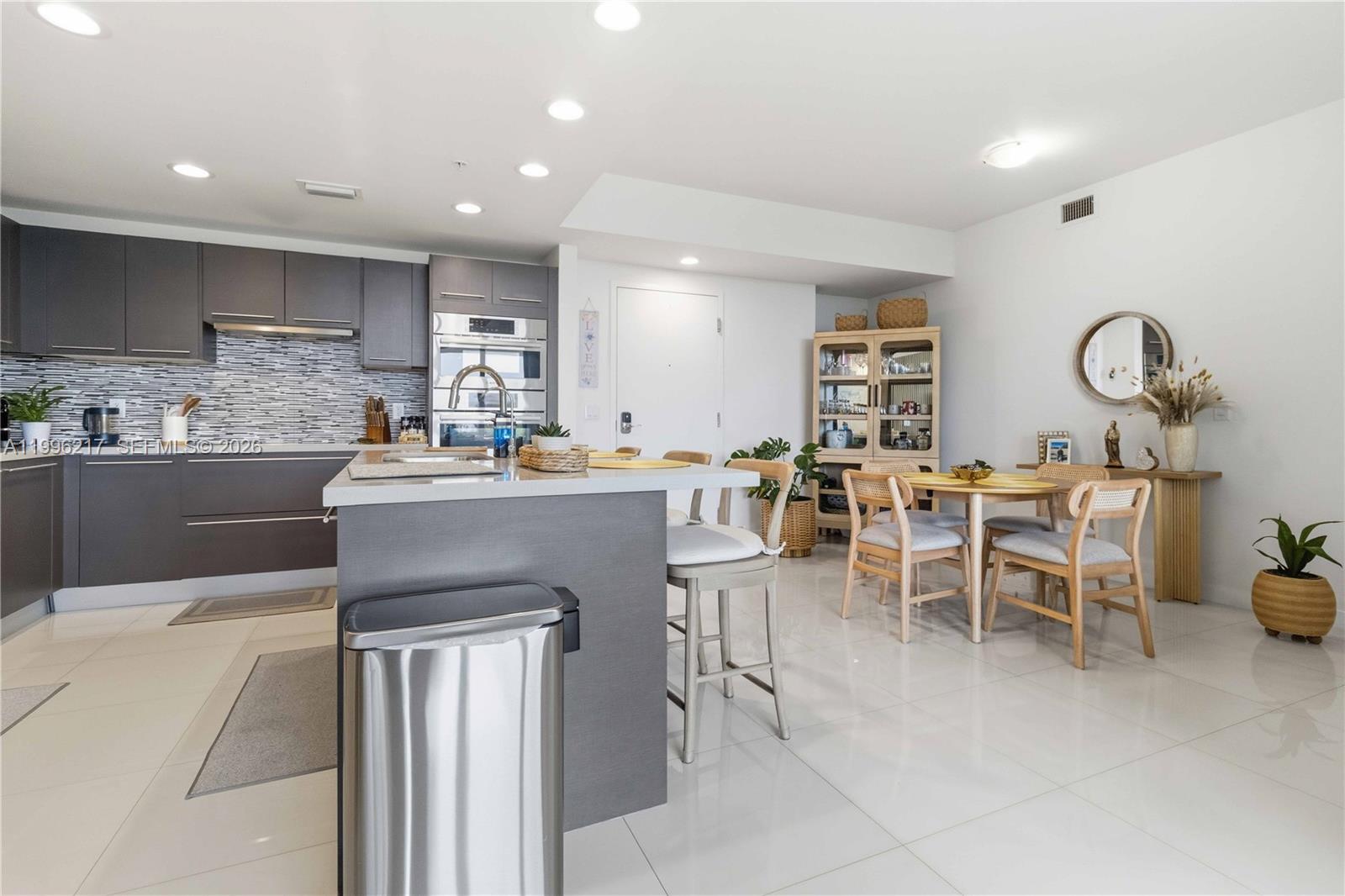 A modern kitchen features dark gray cabinetry, a central island, and an adjacent dining area — 7875 NW 107th Ave # 310, Doral FL 33178, DORAL, FL