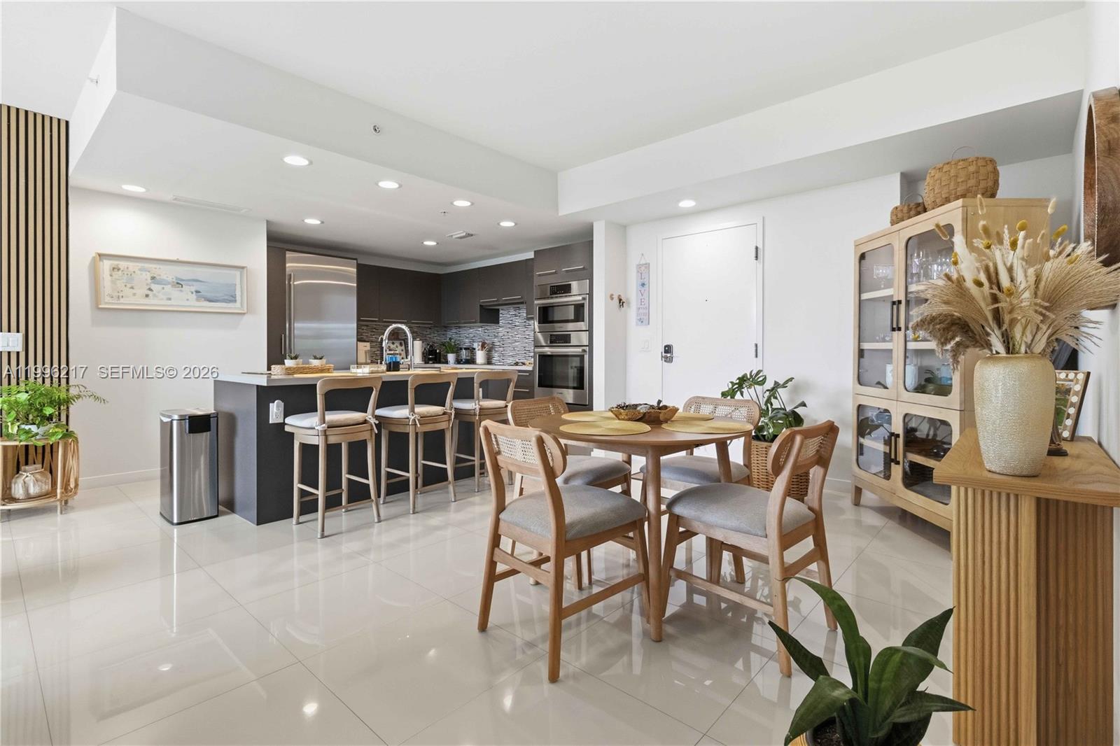 A modern kitchen and dining area feature light tile floors, wooden furniture, and stainless appliances — 7875 NW 107th Ave # 310, Doral FL 33178, DORAL, FL