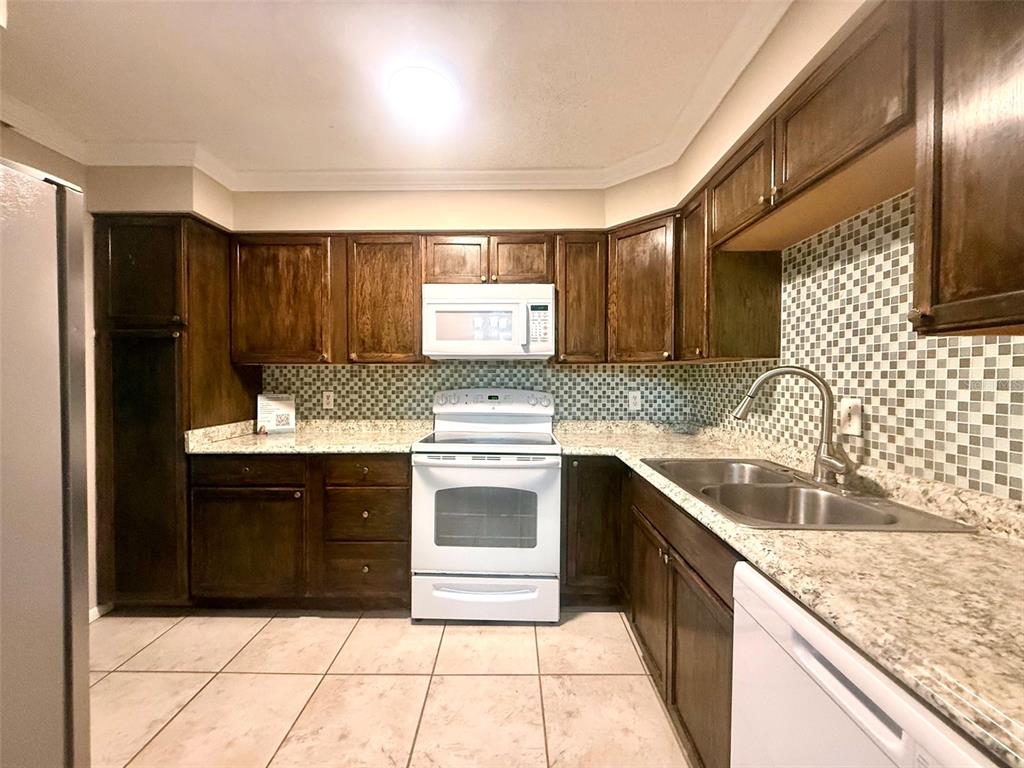 A kitchen features dark wood cabinets, white appliances, a tiled backsplash, and granite-look countertops — 534 ORANGE DRIVE UNIT 27, ALTAMONTE SPRINGS, FL