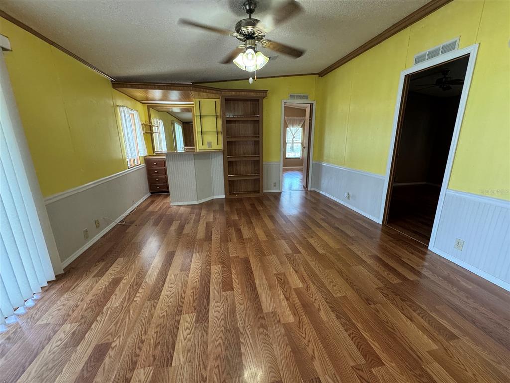 A living room features yellow walls, wood-look flooring, a ceiling fan, and a built-in bar — 5310 TIGERS TAIL, LEESBURG, FL