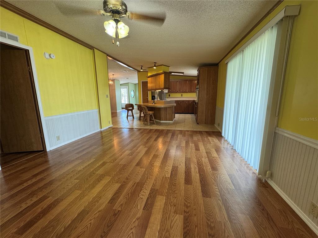 A living room with wood flooring leads to an open kitchen with a breakfast bar — 5310 TIGERS TAIL, LEESBURG, FL