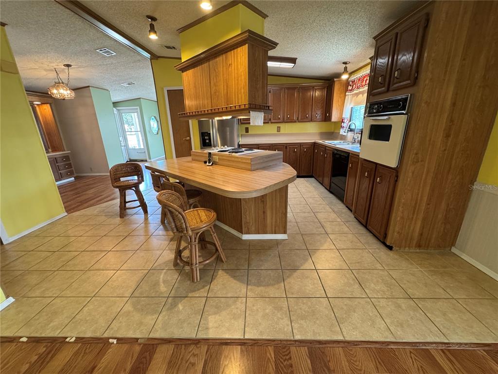 A kitchen features wood cabinets, a central island with a cooktop, and tile flooring — 5310 TIGERS TAIL, LEESBURG, FL