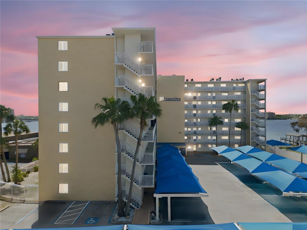 An exterior view of a multi-story apartment building with a parking lot and blue awnings — 145 N HALIFAX AVENUE UNIT 602, DAYTONA BEACH, FL