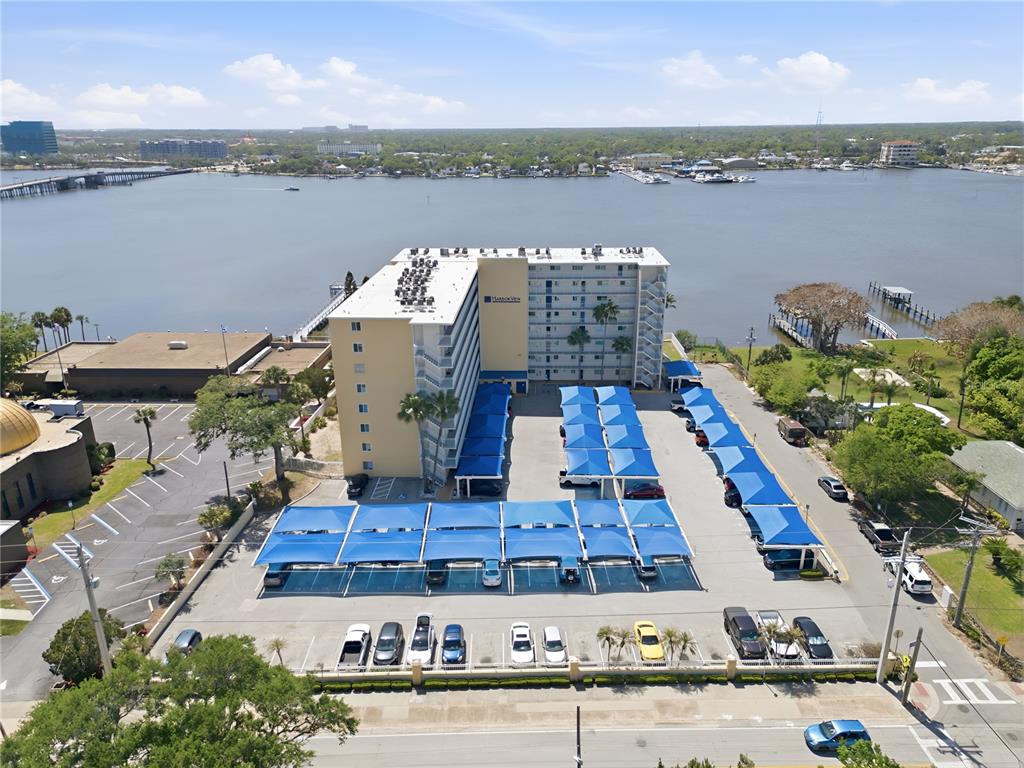 An aerial view shows a multi-story apartment building with covered parking and a waterfront location — 145 N HALIFAX AVENUE UNIT 602, DAYTONA BEACH, FL