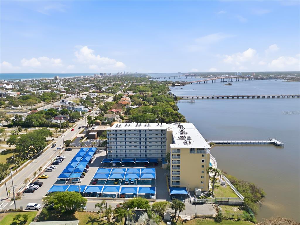An aerial view shows a multi-story apartment building with covered parking next to a bay — 145 N HALIFAX AVENUE UNIT 602, DAYTONA BEACH, FL