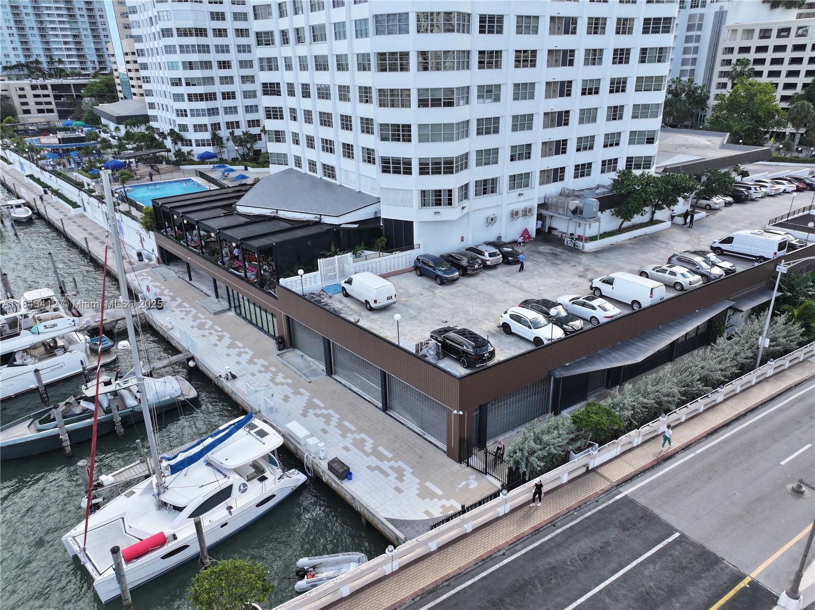 An aerial view shows a waterfront building with a parking deck, boats, and a pool — 801 Brickell Bay Dr, Miami FL 33131, MIAMI, FL