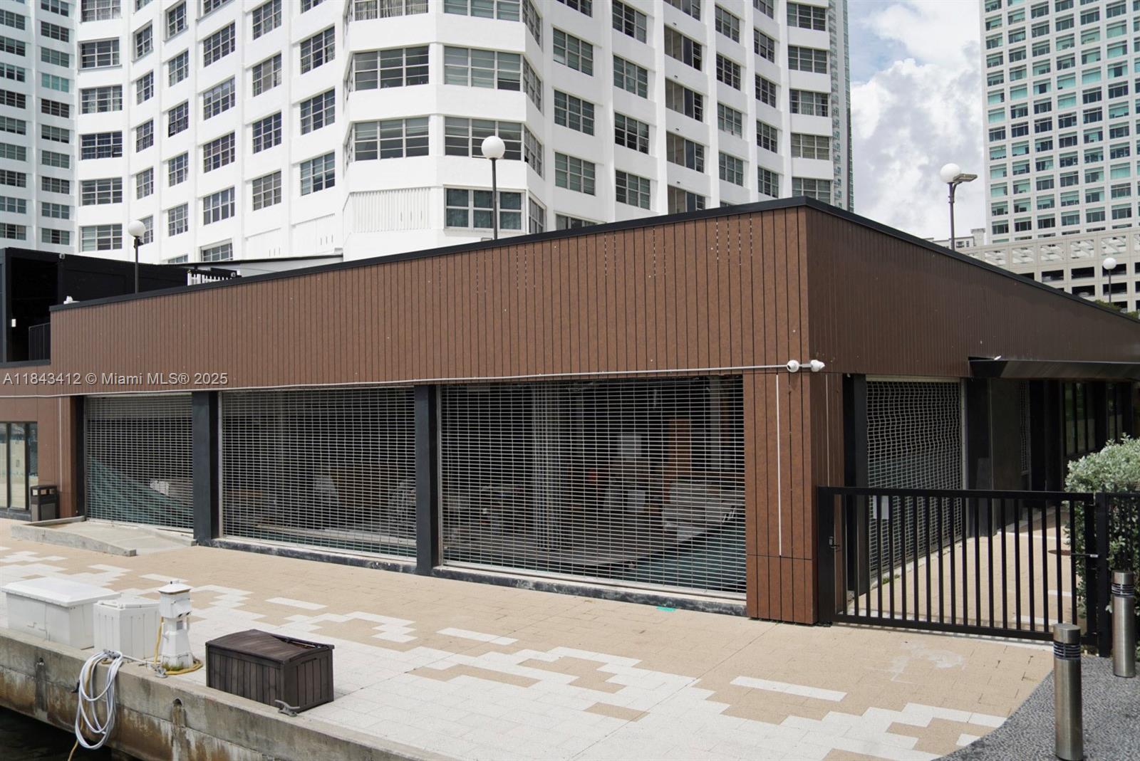 A low-rise building with brown siding and metal security grilles sits along a paved waterfront — 801 Brickell Bay Dr, Miami FL 33131, MIAMI, FL