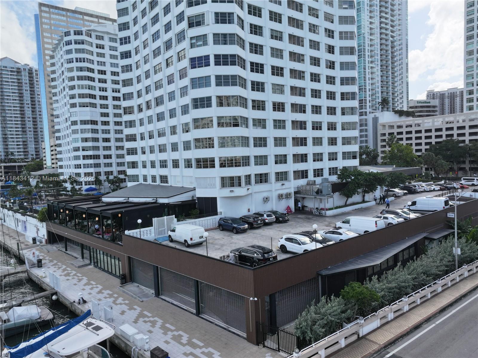 An elevated view shows a white high-rise building with an attached parking deck and waterfront — 801 Brickell Bay Dr, Miami FL 33131, MIAMI, FL
