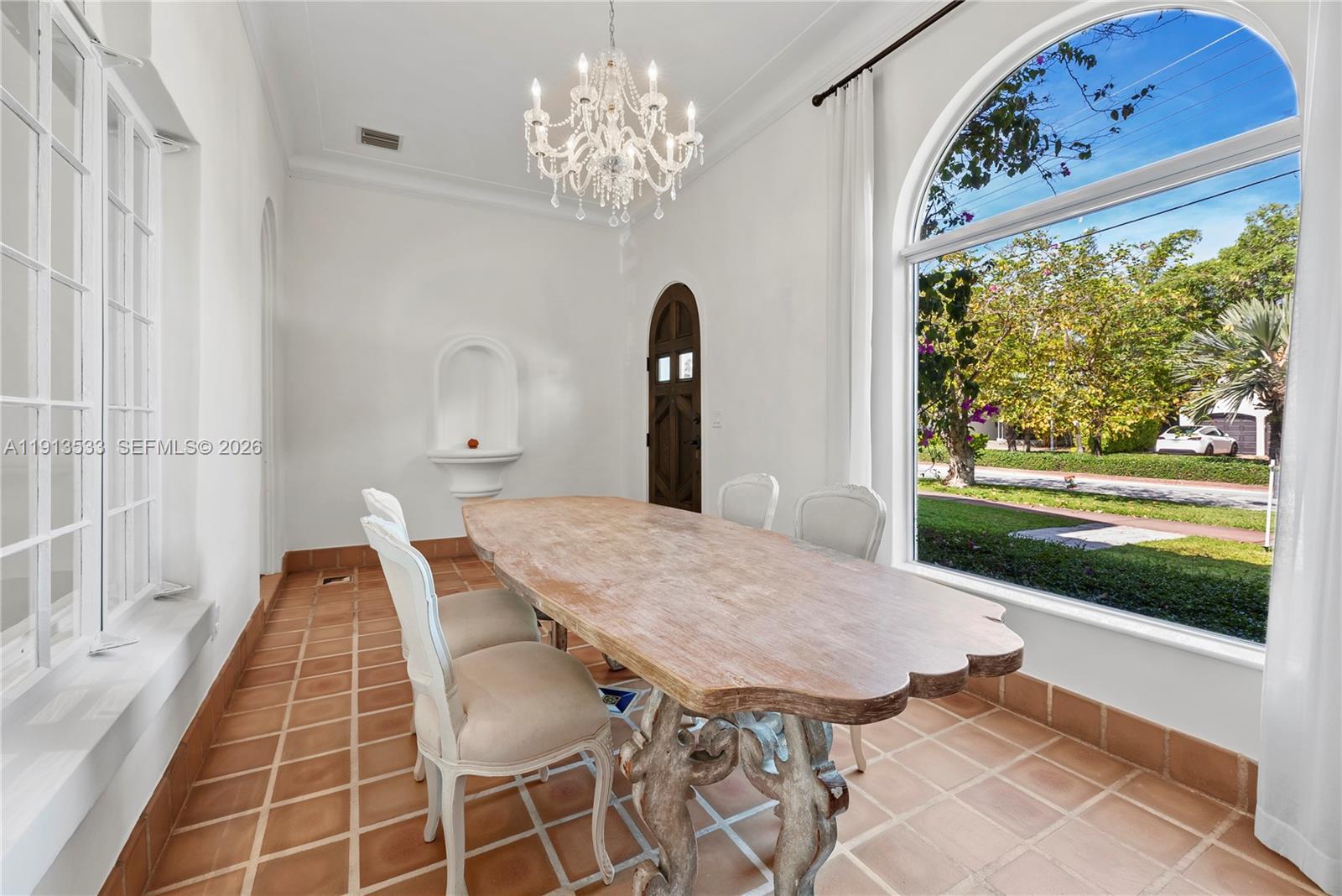 A dining room features a wooden table, chandelier, arched window, and terracotta tile flooring — 5800 La Gorce Dr, Miami Beach FL 33140, MIAMI BEACH, FL