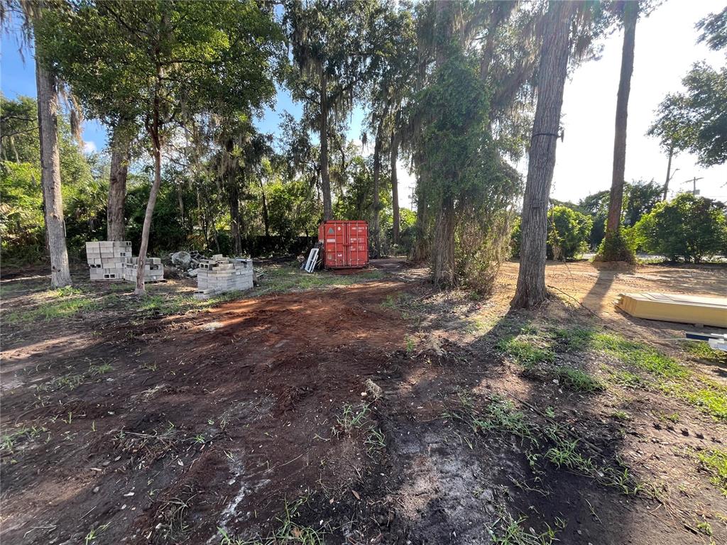 A vacant, wooded lot features stacks of concrete blocks and a red shipping container — 1222 NW 2ND STREET, GAINESVILLE, FL