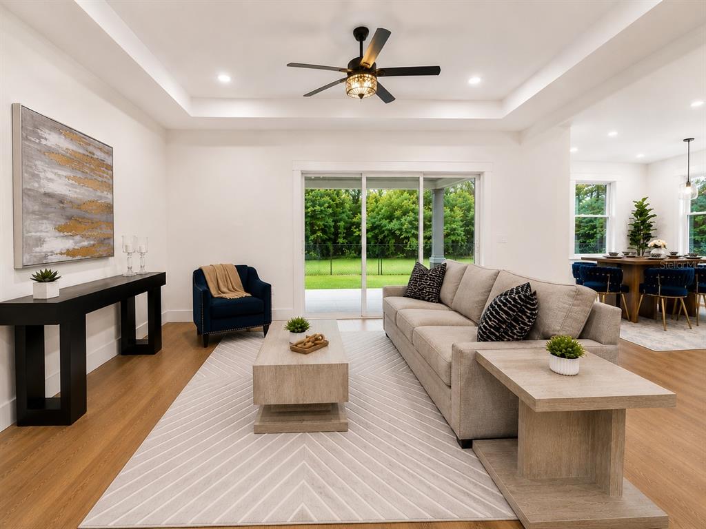 A living room with a tray ceiling, beige sofa, blue armchair, and sliding glass doors — 1835 ROOSEVELT AVENUE, SANFORD, FL