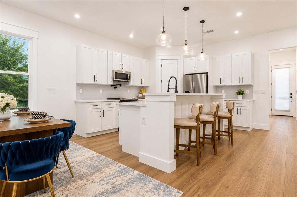 A modern kitchen features white cabinetry, a central island with bar seating, and wood flooring — 1835 ROOSEVELT AVENUE, SANFORD, FL