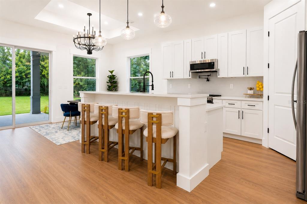 A modern kitchen features white cabinetry, a breakfast bar with four stools, and sliding doors — 1835 ROOSEVELT AVENUE, SANFORD, FL
