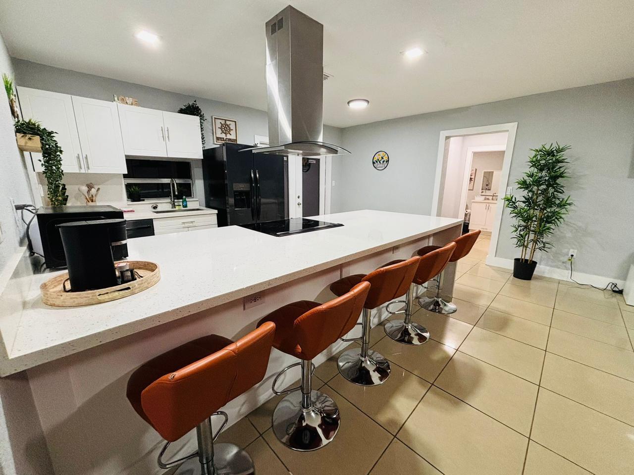 A modern kitchen features a large white quartz island with orange bar stools and cabinetry — 2010 NE 1st Avenue, Pompano Beach FL 33060, POMPANO BEACH, FL