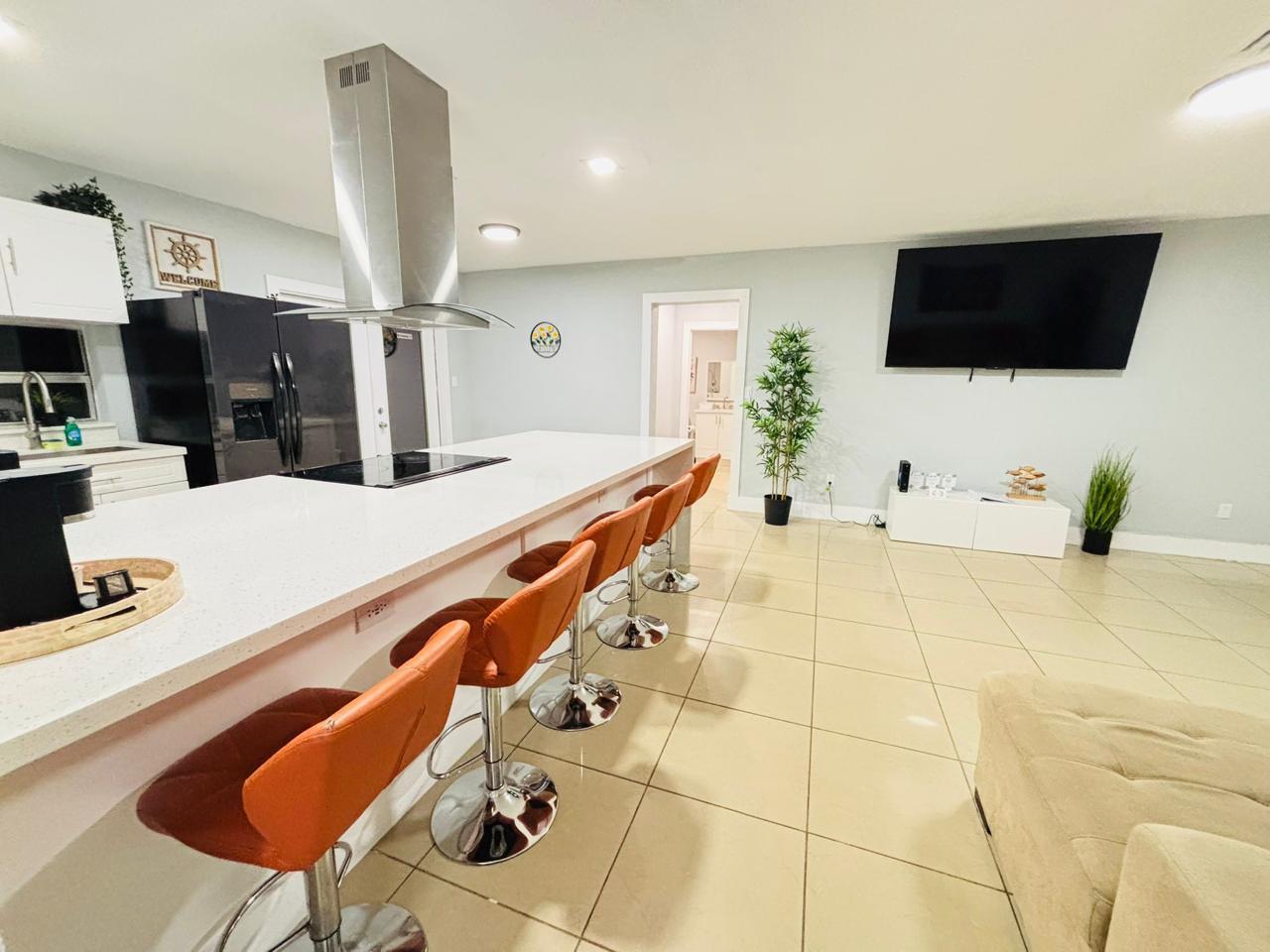 A kitchen with a long white island, orange bar stools, and an adjacent living area — 2010 NE 1st Avenue, Pompano Beach FL 33060, POMPANO BEACH, FL
