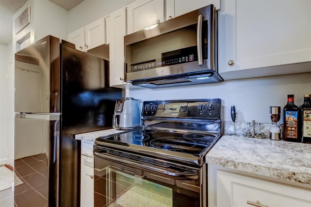 A kitchen features white cabinets, a black refrigerator, a black stove, and a microwave — 2333 FEATHER SOUND DRIVE UNIT B211, CLEARWATER, FL