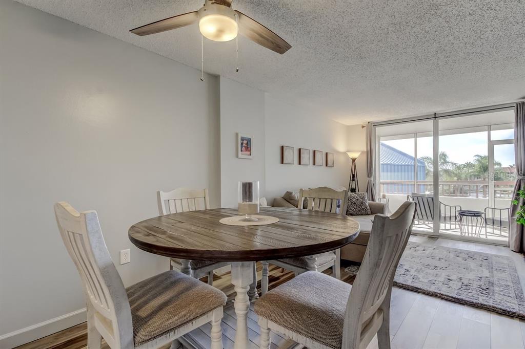 A dining area with a round wooden table and chairs sits before a living room balcony — 2333 FEATHER SOUND DRIVE UNIT B211, CLEARWATER, FL