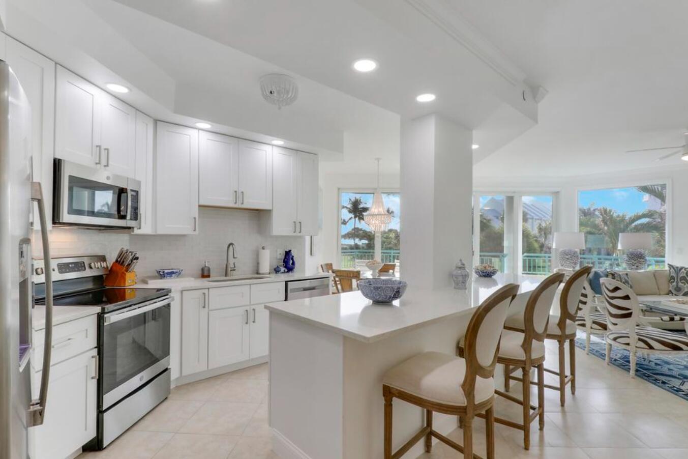 A bright kitchen features white cabinets, stainless steel appliances, a quartz island, and bar seating — 2000 S Highway A1a Highway # N104, Jupiter FL 33477, JUPITER, FL