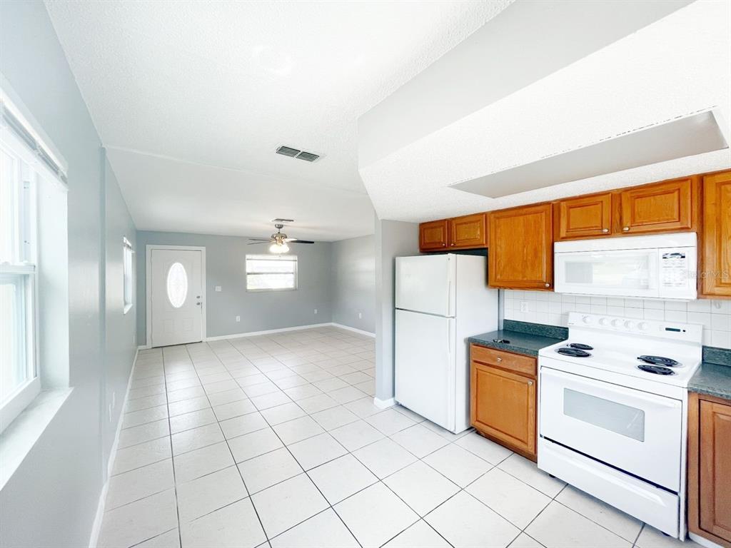 A kitchen with white appliances and wood cabinets opens into a tiled living area — 1551 SWORDBILL DRIVE, HOLIDAY, FL