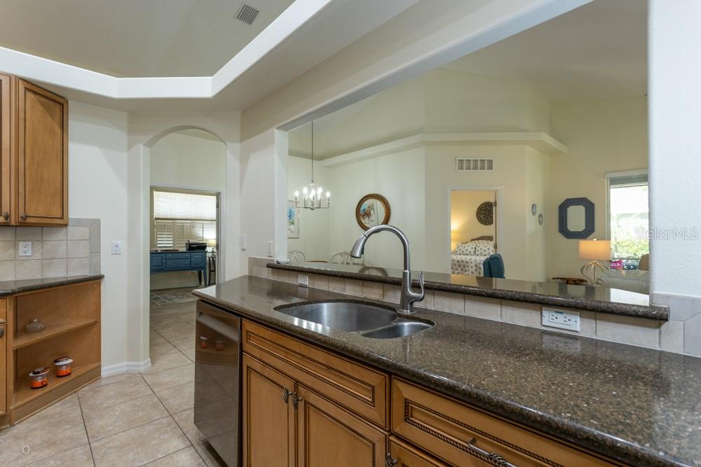 A kitchen features brown granite countertops, wood cabinets, and a sink overlooking an adjacent room — 150 W WATERSIDE PARKWAY, PALM COAST, FL