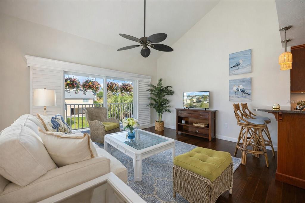 A living room with a vaulted ceiling, ceiling fan, white sofa, and a balcony view — 109 BAYSHORE ROAD UNIT 10, NOKOMIS, FL