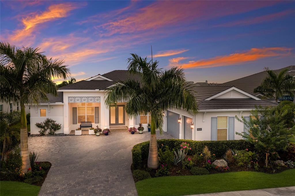 A single-story house with a paved driveway, palm trees, and a sunset sky — 8448 CANE BAY COURT, LAKEWOOD RANCH, FL